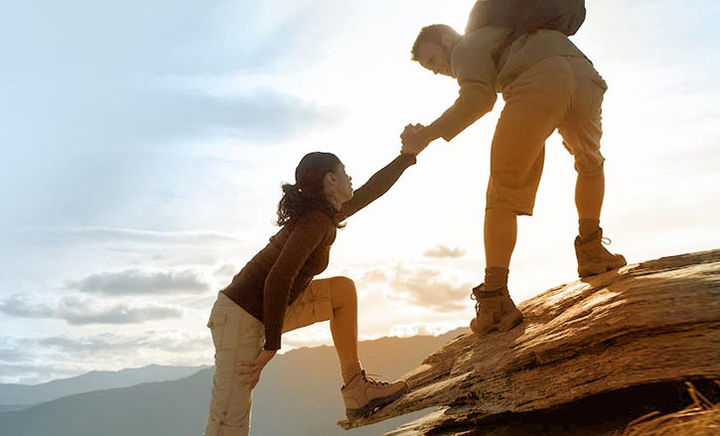 Mann hilft Frau beim Aufstieg auf Berggipfel